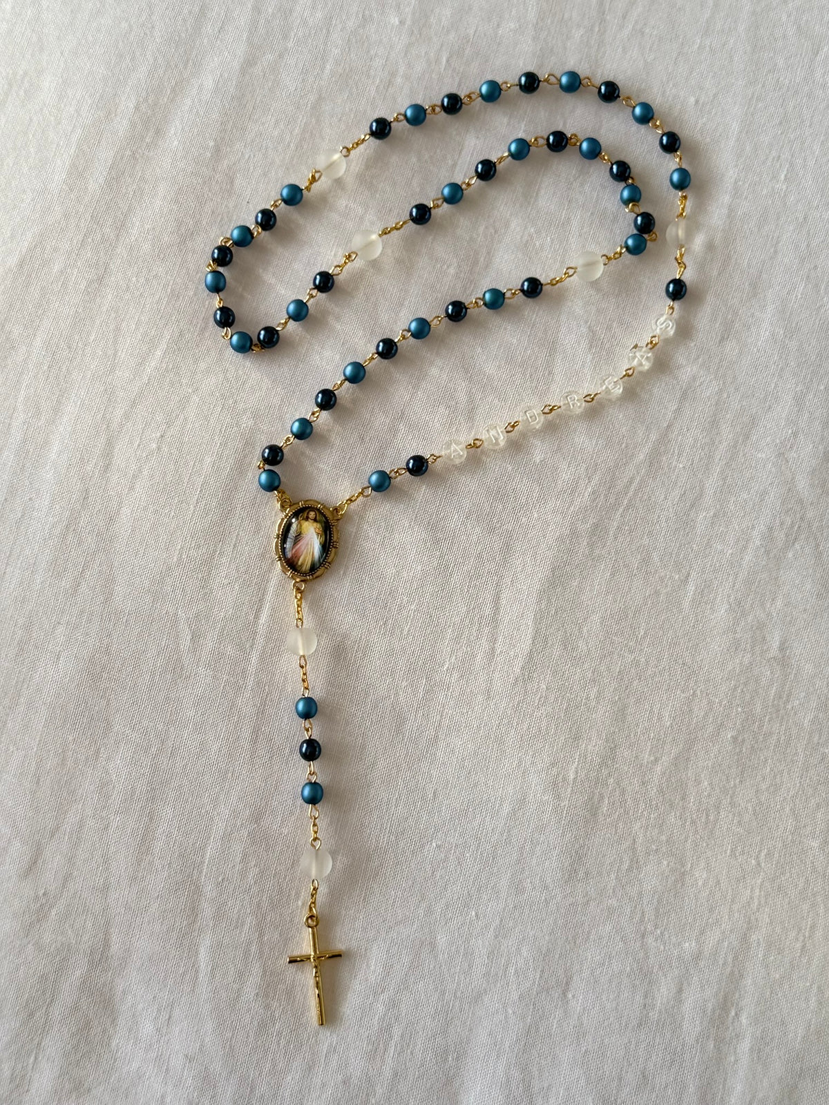 Rosary necklace with blue beads and a cross on a light gray background