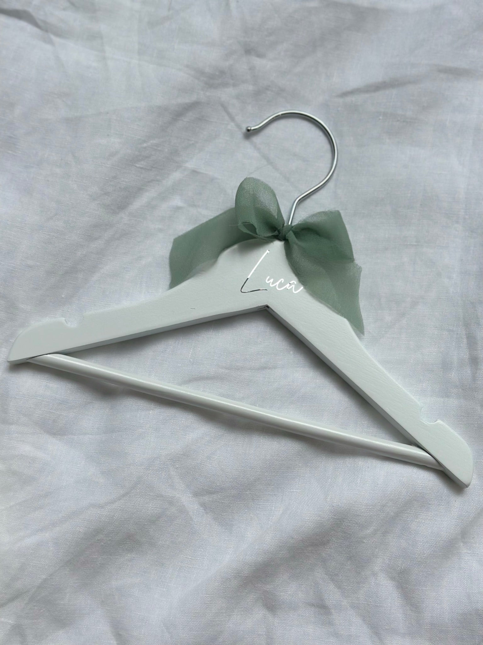 White hanger with a green bow on a gray fabric background
